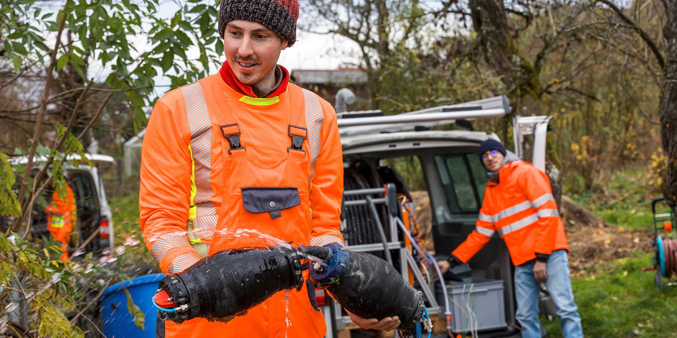 A man in a orange overall carries the two black sealing elements with both of his hands