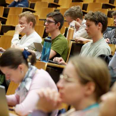 Students in a lecture hall, in focus is a man with glasses and a green T-shirt