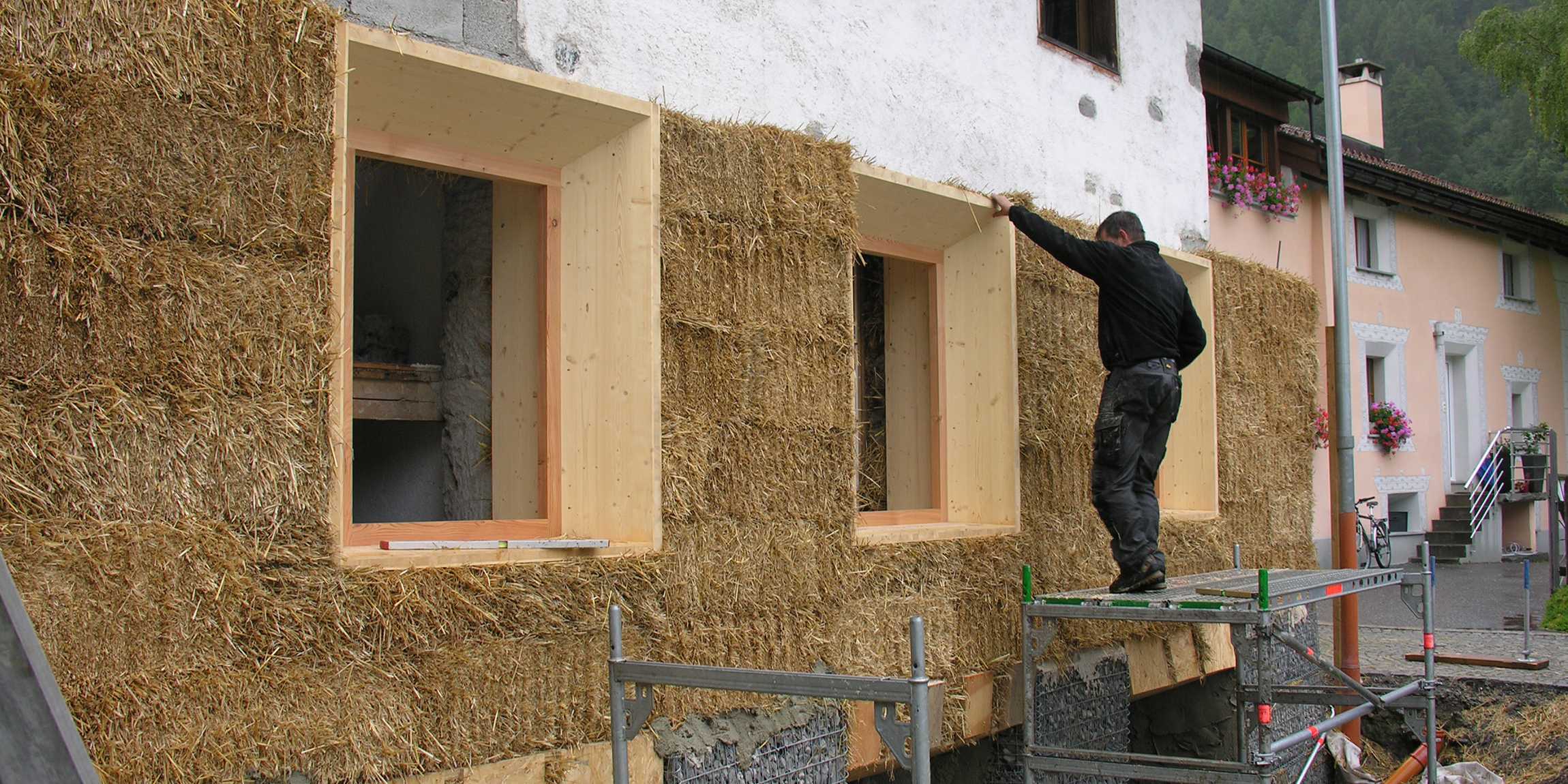 Ein Mann arbeitet an einer Hausfassade mit Stroh.