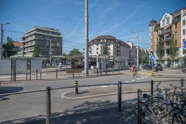 Velos, welche abgestellt sind. Daneben ist direkt eine Strasse und im Hintergrund die Tramhaltestelle des Albisriederplatzes sichtbar.